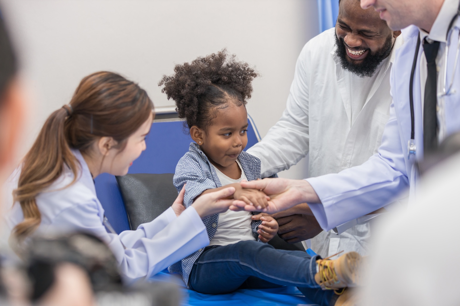A child is seen by a doctor in a hospital while her parent smiles on.